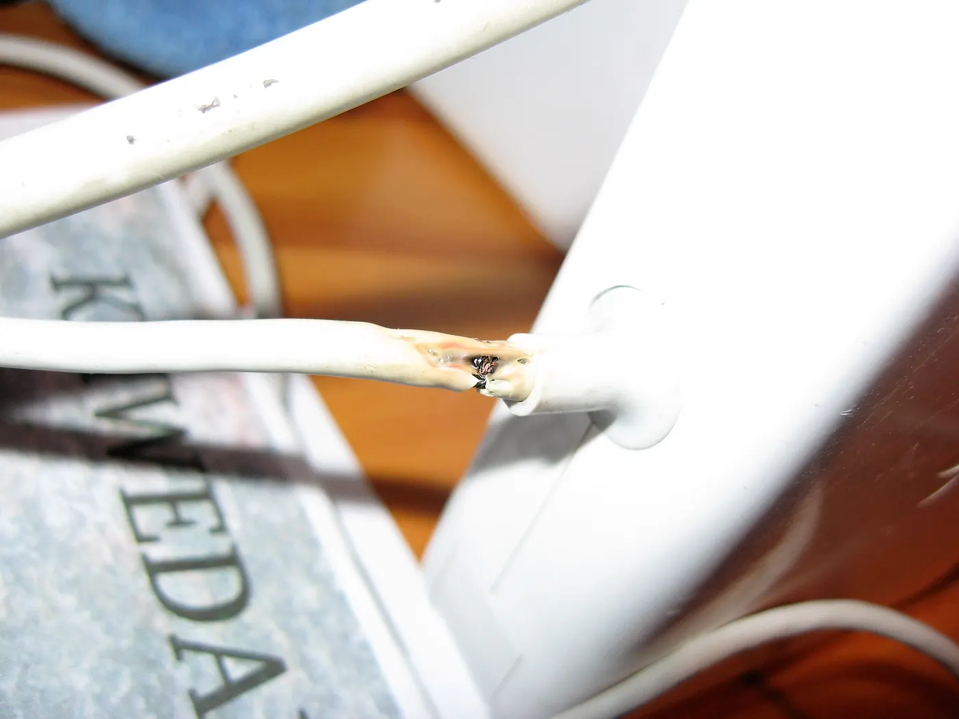 A white MagSafe power cable with its insulation split open where it leaves the power brick